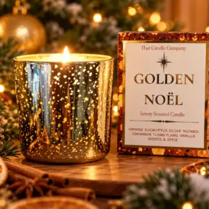 Golden Noël luxury scented Christmas candle burning in a gold-speckled glass jar beside its gift box with festive decorations.